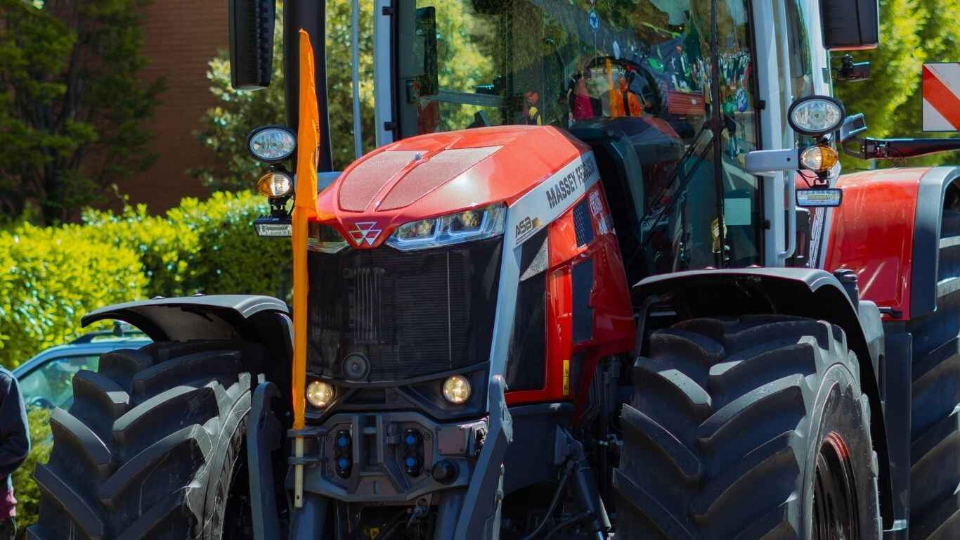 A close-up side-view of the Massey Ferguson MF 5M tractor, highlighting the distinct red and gray colors and the new MF logo on the hood.